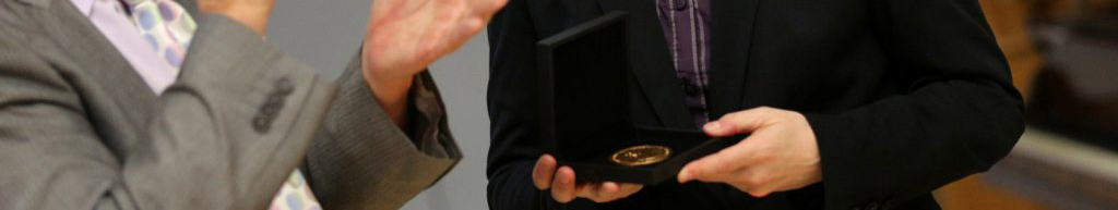 Personal holding gold medal in presentation case whilst another person claps