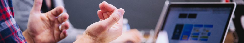 Two hands in an open gesture next to a laptop screen