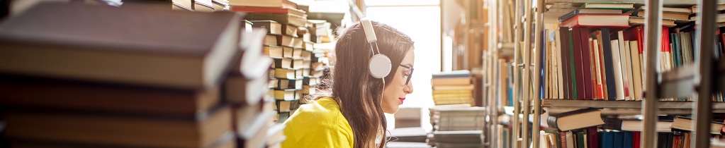 Young woman listening to the music sitting on a heap of books in a library