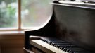 An antique piano sits by a rustic window