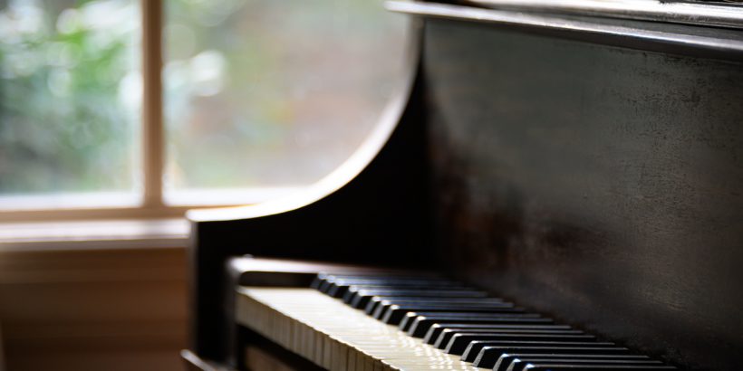 An antique piano sits by a rustic window